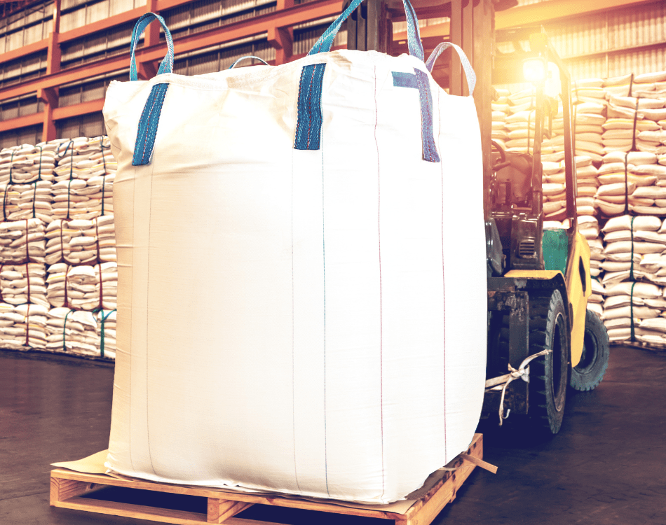 A large white polypropylene bulk bag on a wooden pallet with stacks of similar bags in the background, illustrating the benefits in materials handling of understanding the differences between polypropylene and PVC bulk bags.